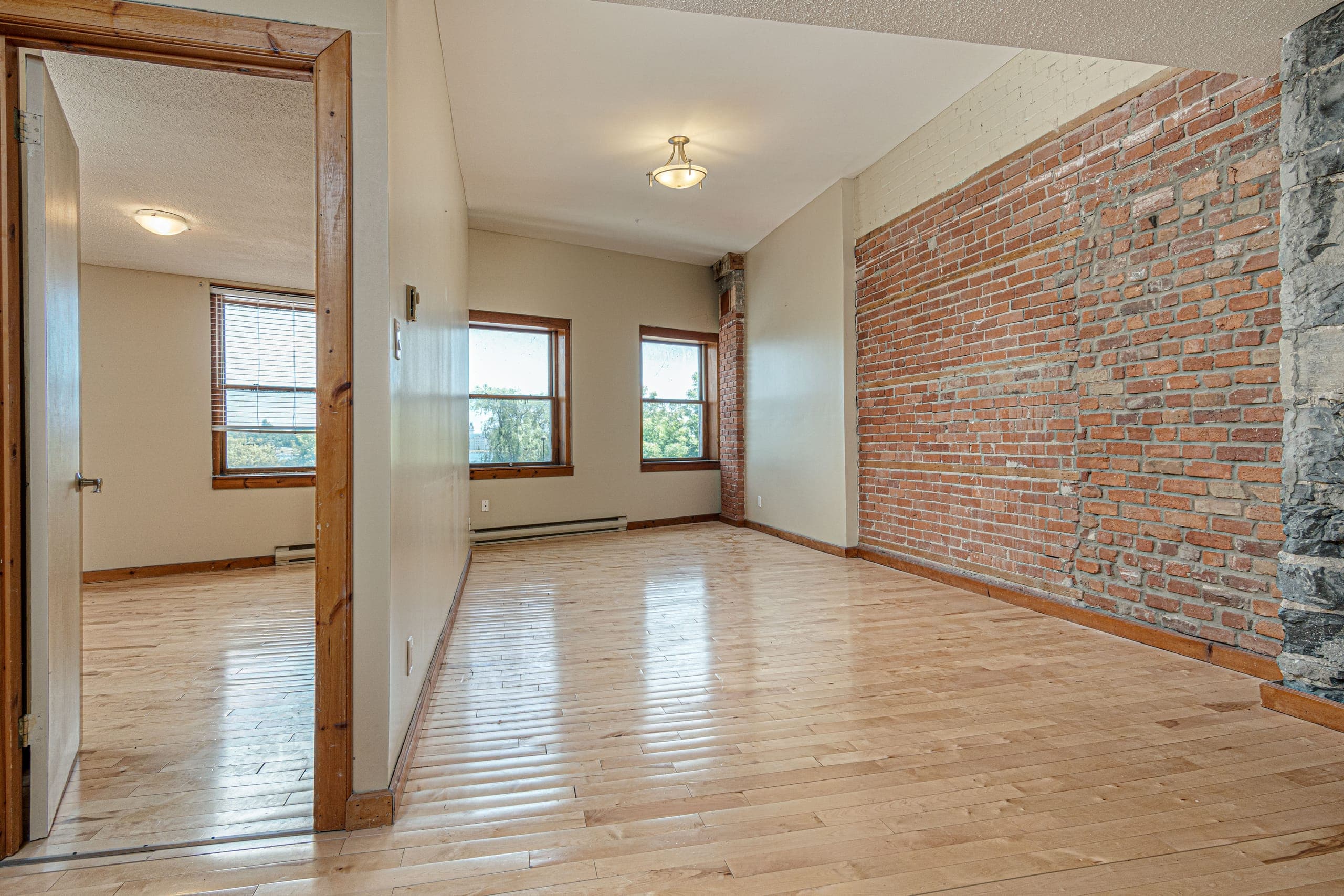 Living space at 265 Ontario with an exposed brick wall, a stone column, three windows and hardwood floors